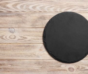 Black slate round stone on wooden background, top view, copy space.